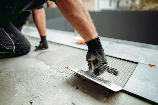 Flooring and tiling. Hand of professional construction worker placing floor tiles on adhesive surface on balcony