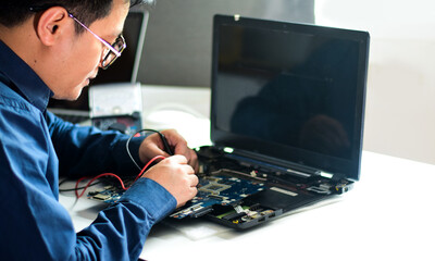 young man who is a computer technician A laptop motherboard repairman is using an IC meter to look...