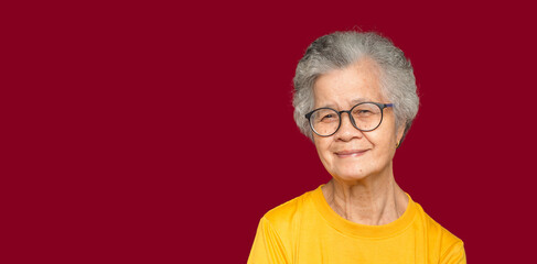 Portrait of an elderly Asian woman with short gray hair looking at the camera with a smile while standing on a red background