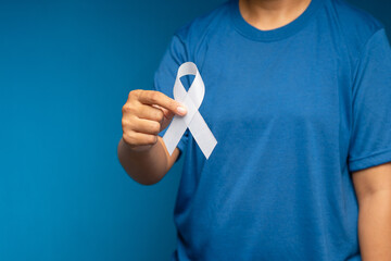 A female hand is holding a white ribbon on a blue background - obrazy, fototapety, plakaty