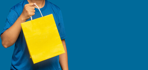 Hand holding a yellow shopping bag with a handle while standing on a blue background