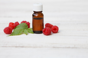 Red Raspberry (rubus idaeus) seed oil bottle with red raspberry and leave on white wooden background