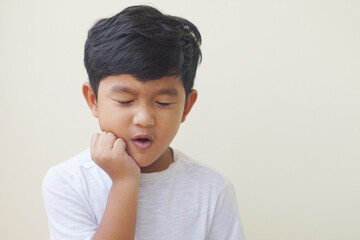 Little Asian boy 5 year old suffering from toothache pain while eating candy, holding his cheek, dental pain and he feel so sad. 