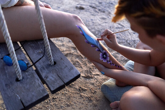 Artist painting a flower in the leg of a woman on the beach