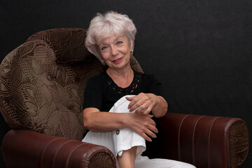 Portrait of a beautiful and smiling elderly blonde woman 60-65 years old, sitting in a chair on a...