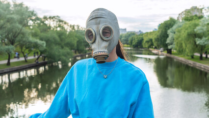 A girl in a gas mask stands on a bridge across the river. Alienation in the city. Fashion, ecology...