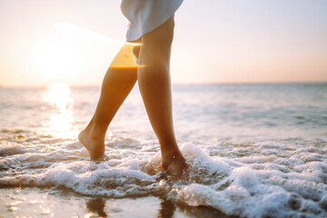 Close- up leg of young woman walking along wave of sea water and sand on the summer beach. The concept of relax, travel, freedom and summer vacation.