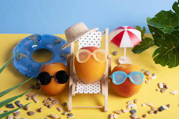 Apricots in sunglasses on the beach in a chaise longue and with inflatable circles.