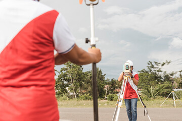 A land surveyor using an optical Total Station to measure the distance from a prism reflector.