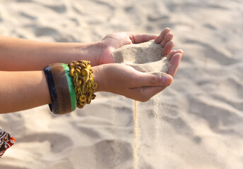 Female hands with many boho bracelets, and sand in the beach.