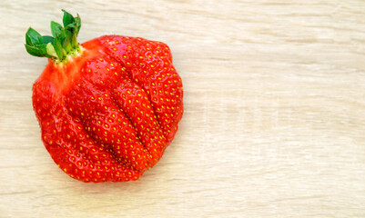 Top view of a big ripe red strawberry, heart shaped on a wooden table.