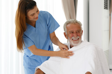 Obraz premium A female nurse uses a blanket to a senior Caucasian man sitting in a wheelchair