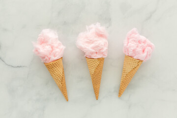 Waffle cones filled with cotton candy against a light marble background.