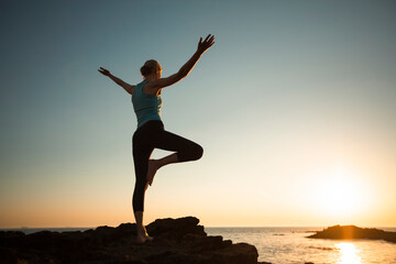 Fototapeta premium A woman performs yoga exercises on the sea beach during sunset.