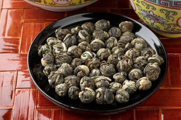 Dried Chinese Jasmine Dragon pearl tea leaves on a black bowl