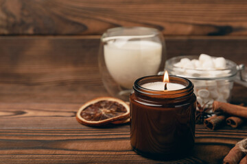 Aromo candle on the background of a cup of hot chocolate and spices with marshmallows for winter drinks on a brown textured table. Winter hot drink. Hot chocolate with marshmallows and spices. Copy sp