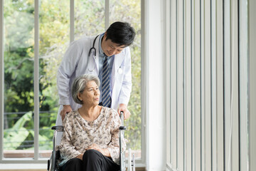 Doctor taking care elderly asian woman on wheelchair at the hospital ward. People and health care...