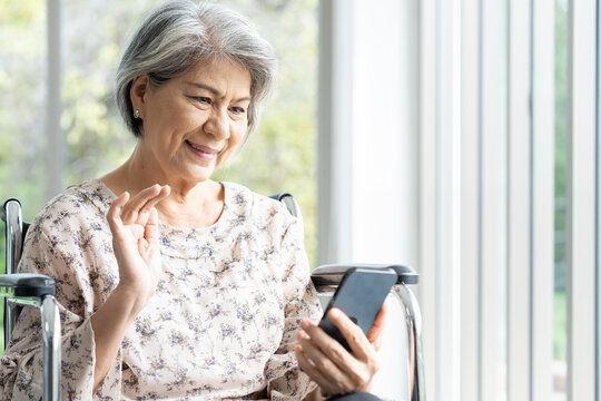 Elderly Asian Woman Using Mobile Phone On Wheelchair At Home. Asian Senior Old Grandma Use Smart Phone While Sit On Wheelchair At Hospital