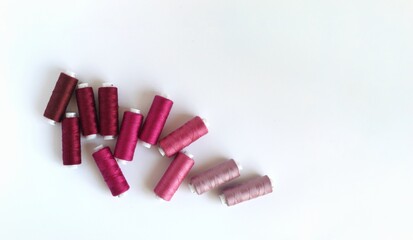 Coils of thread in pink, purple and wine colors. White background, space for text, top view