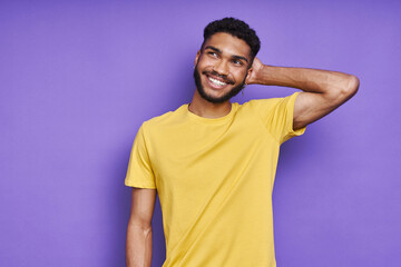 Thoughtful African man holding hand behind head while standing against purple background