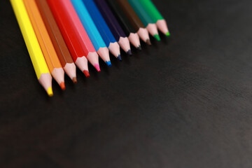 Selective focus. A set of colored pencils on a black wooden background. Sharpened bright pencils. Drawing and learning. Back to school
