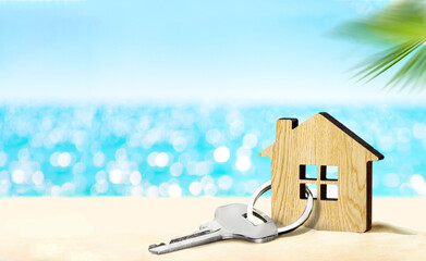 House by the sea concept. Figure of house and key on sandy beach - obrazy, fototapety, plakaty