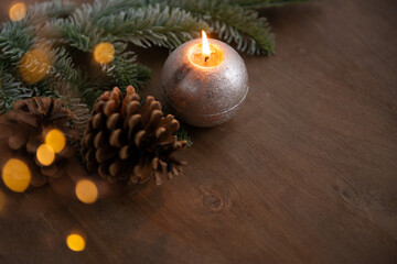Obraz na płótnie Canvas christmas decoration composition with burning candle, cone and lights on natural wooden background