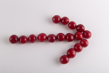 Cherry arrow on white background. Top view on fresh wet red fruits lay in shape of pointer to right.