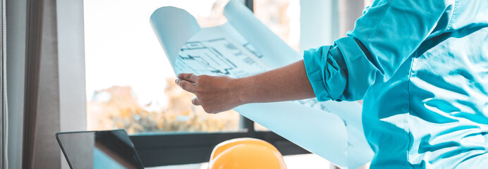 Architectural building design and construction plans with blueprints, Young man was designing a building or architecture with a ruler, pen, pencil, tape measure, architect hat and other equipment.