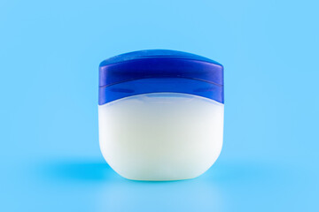 Vaseline or petroleum jelly in a clear jar on blue background with copy space for text. Skin care...
