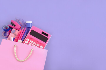 A set of stationery in purple and pink shades for the office is in a pink bag.The concept of online stationery stores for schools, students, accountants, business purchases and sales.Copyspace