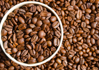 Roasted coffee beans in a paper cup against the background of not sharp coffee beans.