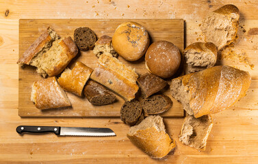 Pieces of cut and torn bread with a knife on wooden board.