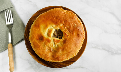 The traditional dish of the peoples of the Caucasus is Karachai khychins (Ossetian pies) with meat in a wooden plate and a fork on a napkin. Light marble background, top view, copy space.