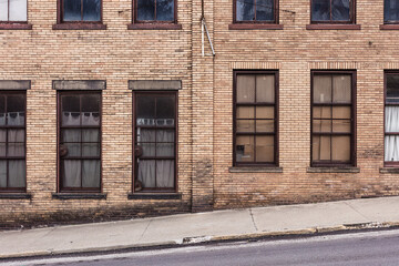 Fototapeta na wymiar Side of vintage brick building with windows covered with metal grates on hill in small midwest town