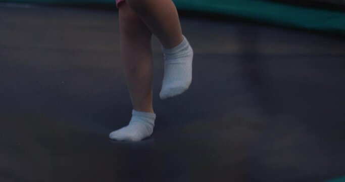 Little girl jumps on trampoline in street on summer day.
