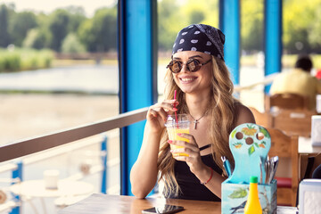Hipster bohemian woman with head scarf and retro sunglasses drinking fresh lemonade at bar terrace