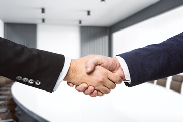 Two businessmen shake hands on the background of bright conference room, investing concept, close up