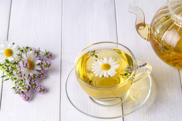 Herbal tea with chamomile and thyme in a transparent cup on a white wooden table
