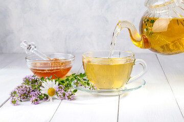 Herbal tea with chamomile and thyme in a transparent cup on a white wooden table