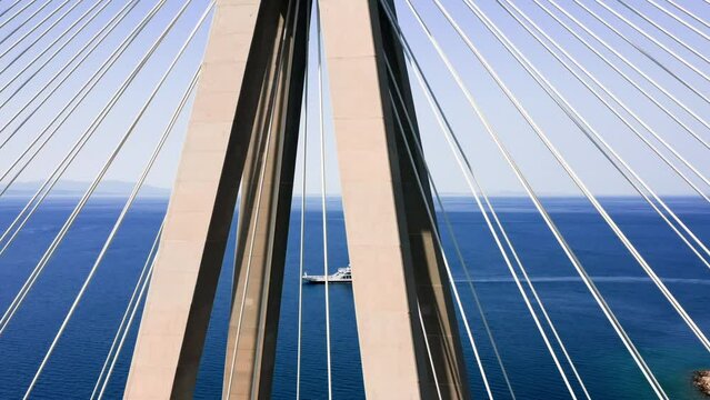 Close up drone shot of pylon of cable strayed bridge over the sea with ferry boat passing by, Rio - Antirio bridge at Peloponnese, Greece.