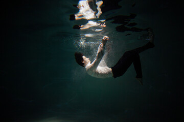 Sink. A young man is going to the bottom. A guy in a white shirt and trousers falls under the water, calmness and acceptance of fate - obrazy, fototapety, plakaty