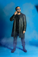 portrait of a man in a studio in a black leather coat. model with a beard on a blue background. trendy luminous glasses on the face