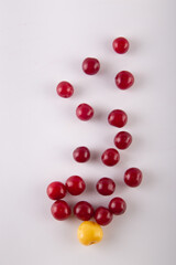 Several red cherries and one yellow scattered on white background. Top view, flat lay. Vertical photo