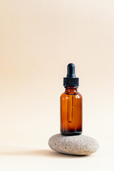 Amber glass dropper bottle with black lid on a podium on stones. Skincare products , natural...