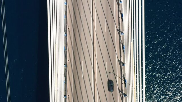 Aerial drone shot of cable strayed bridge over sea and vehicles passing against Antirio town, tilt up camera movement.