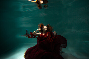 Underwater shooting, a beautiful young woman in a red dress is swimming under the surface of the water. Fabulous photo refraction under water.