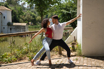 Attractive young couple dancing sensual bachata in an outdoor park with a river in the background....