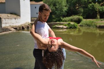 Attractive young couple dancing sensual bachata on a stone floor, in an outdoor park, next to a river. Latin dance concept, sensual, folkloric, urban.