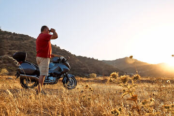 On the road. Tourist man traveling on motorcycle, stopped for looking through binoculars at the...